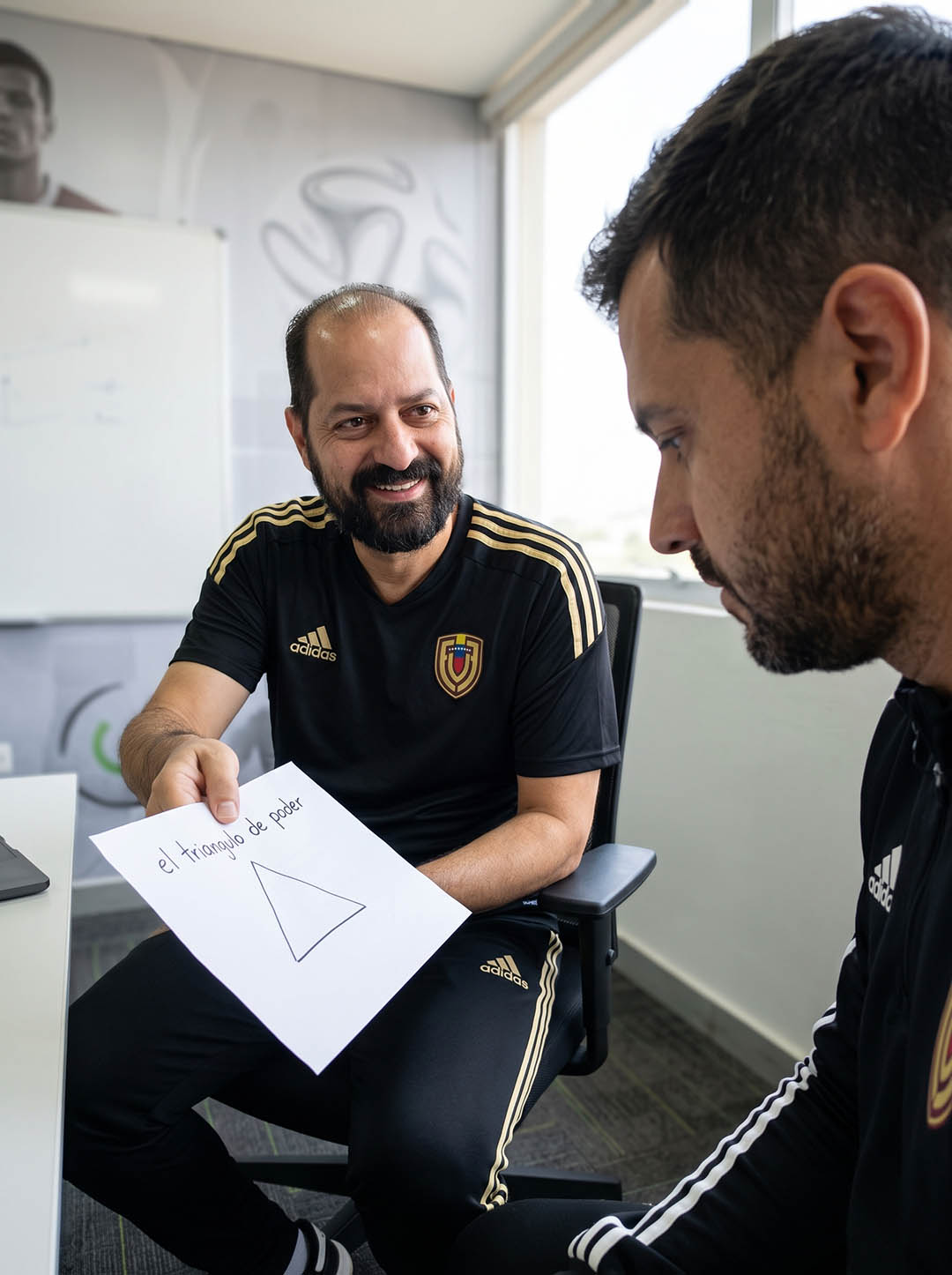 Coach deportivo conversa con un profesional del fútbol durante una sesión de reflexión y autoconocimiento sobre liderazgo y rendimiento.